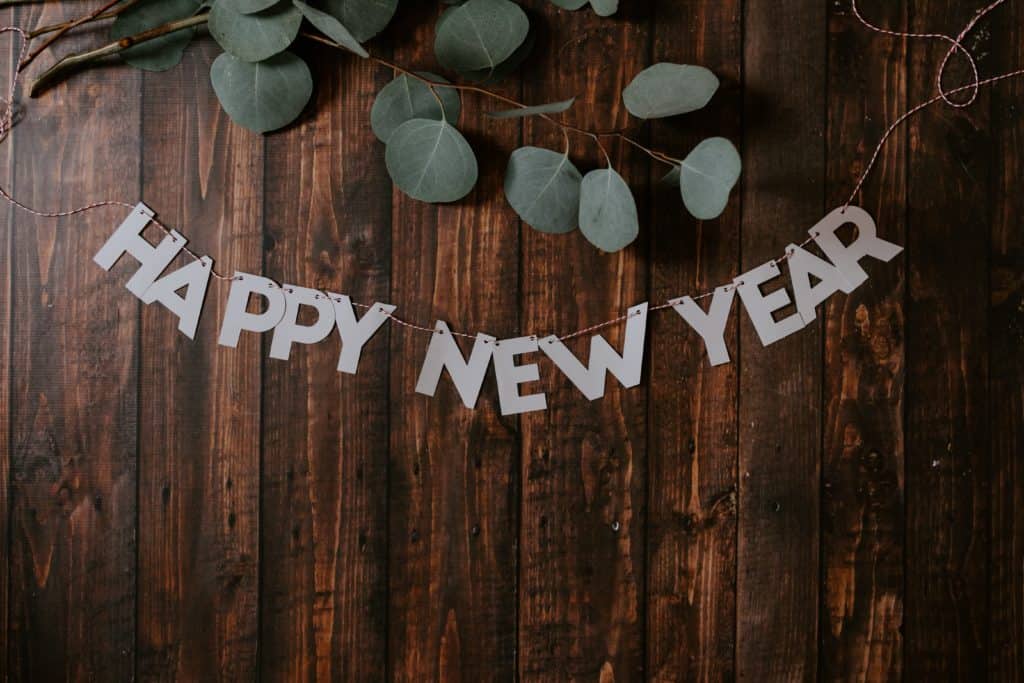 An image of a sign noting Happy New Years on a wood fence with green florals